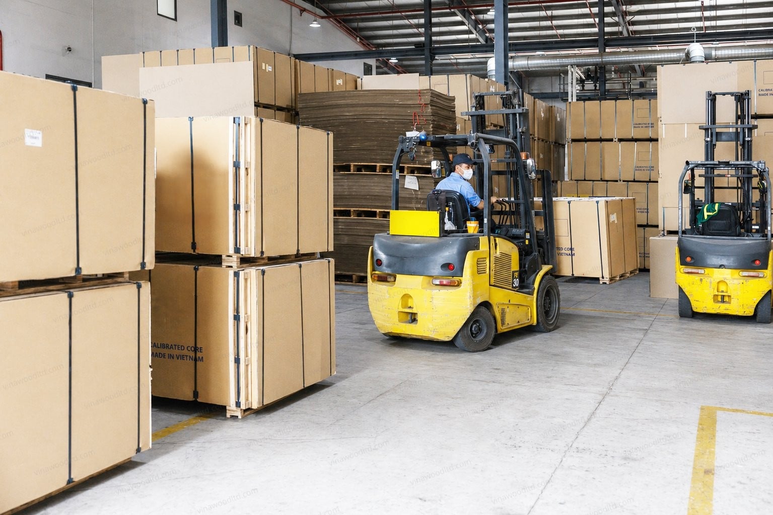 Forklifts loading stacked bundles of finished plywood inside a Vietnamese mill warehouse ahead of export